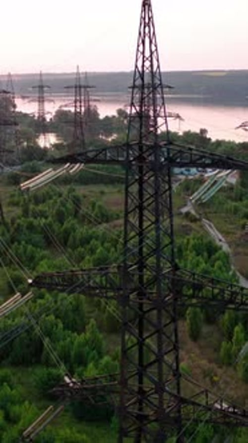 Structure of high-voltage lines outside the city at sunset. Trees and river. Camera motion back.
