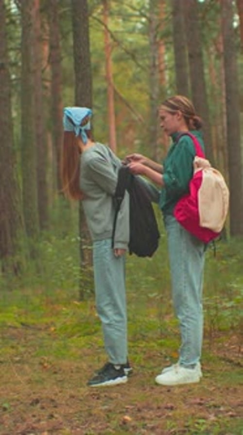 Two Women Hiking As One Helps Other Put on Backpack in Serene Forest