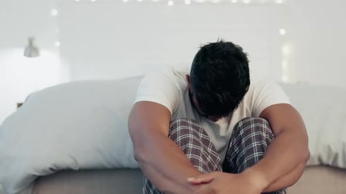 Man Sitting with Knees to Chest in Bedroom