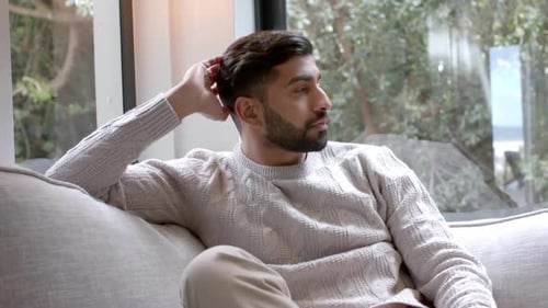 Porträt eines glücklichen, gemischten Mannes, der auf dem Sofa sitzt und zu Hause lächelt, Zeitlupe