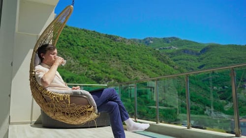 Young Man Relaxing on the Balcony Drinking Coffee Surrounded By Mountain Scenery
