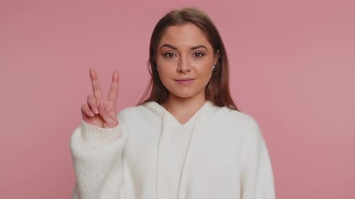 Young Woman Making Peace Sign Against Pink Background