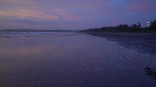 Seascape view of ocean waves crashing on the sandy coastline, during a bright purple sunset, on a cl
