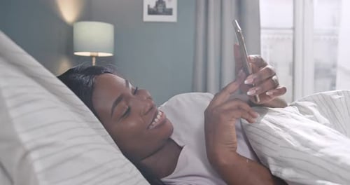 Woman Smiling in Bed Using Her Smartphone
