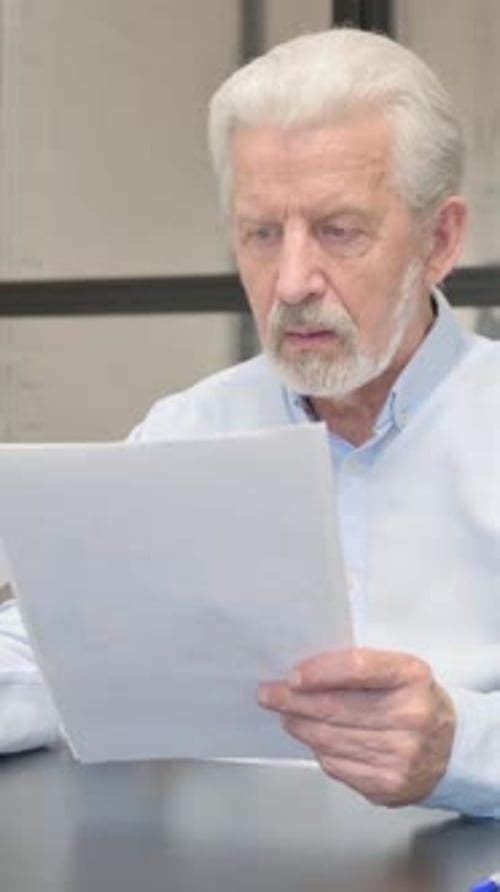Senior Man Reacting to Good News Document at Desk