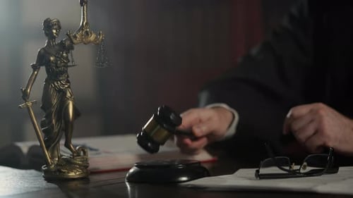Judge Strikes Wooden Gavel on Desk While Statue of Justice Stands in the Background Courtroom