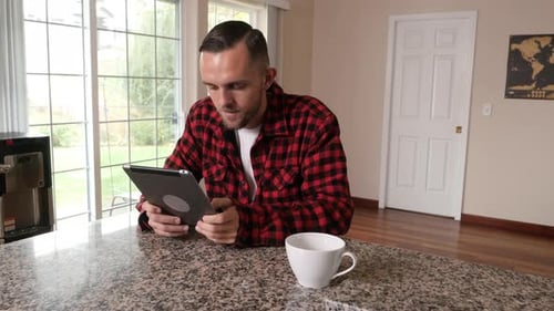 Man Uses Tablet and Drinks Coffee at Counter