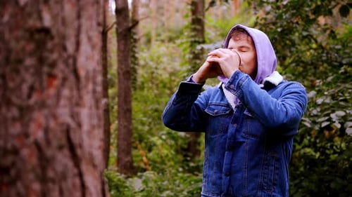 Young Man in Warm Clothes Drinking Coffee From Paper Cup Standing in Forest