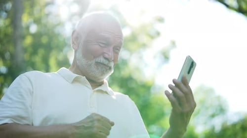 Lowangle View of Cheerful Elderly Man with Long White Beard Enjoying Using Smartphone Watching Funny
