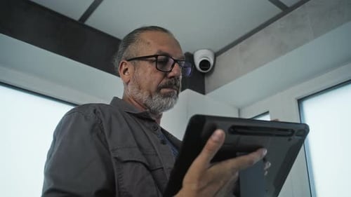 Man Adjusts Security Camera While Using Tablet