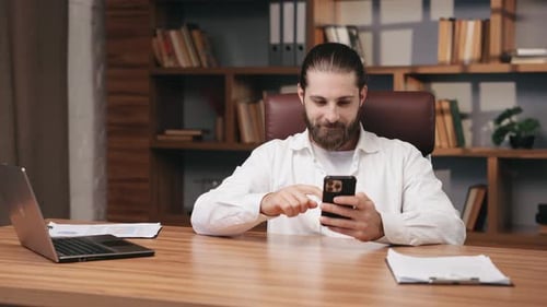 Smiling Entrepreneur Browsing Internet with Smartphone at Home Office