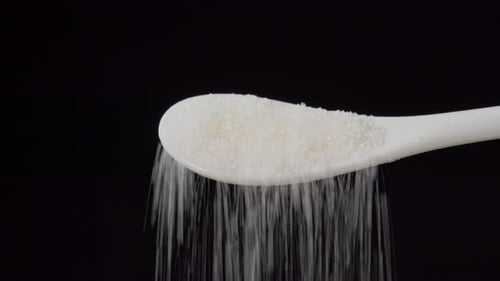 Spoon of sugar pours down isolated on black background. Sugar falling from spoon. Sweet unhealthy