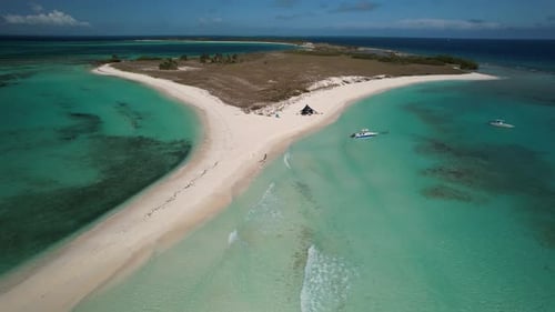 A tropical island with turquoise waters, a boat, and a beach tent, aerial view