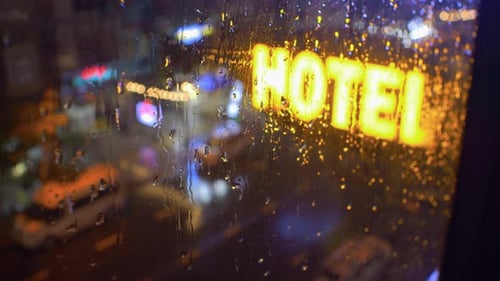 Big neon hotel sign in street below. View from building window. Rain in the city
