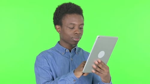 Young African Man Celebrating Success on Tablet on Green Background