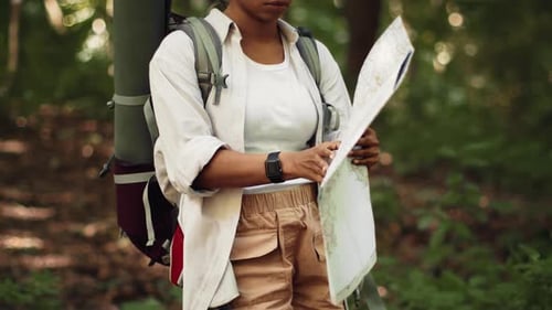 Woman With Dark Skin Reviews a Map While Exploring a Forested Area During the Day