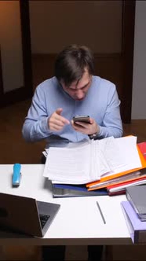 Vertical Video Stressed Office Worker Throwing Phone at Work with Folders and Laptop