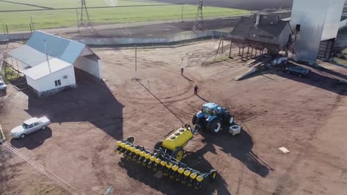 Blue tractor with yellow seeder working on the field in Ukraine OA