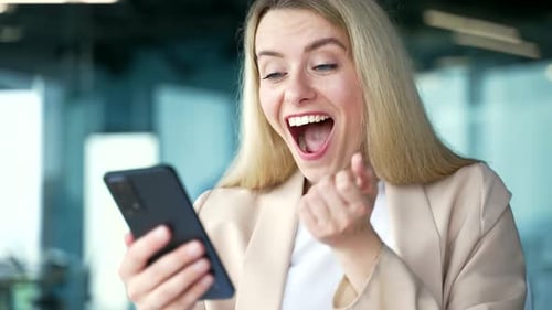 Close up. Happy excited young businesswoman in a suit read great news on smartphone while sitting