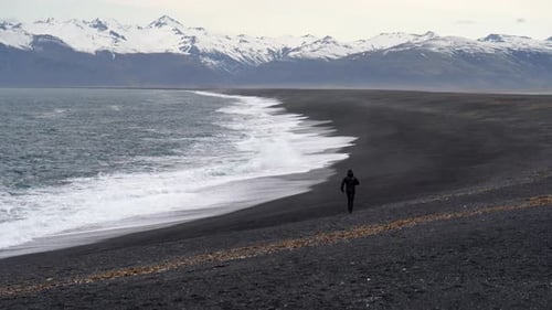 Man Running Along Black Sand Beach By Sea
