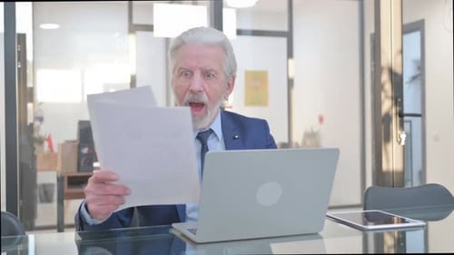 Senior Businessman Celebrating Success at Office Desk