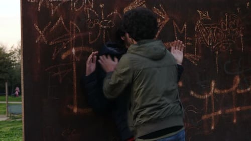 Men Fighting in Park Next to Graffiti Wall