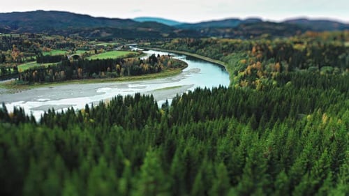 A shallow winding river with a sandy bottom meanders through a lush valley surrounded by autumn-colo