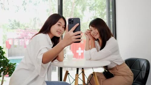 Asian woman and friend using smartphone selfie together in coffee shop.