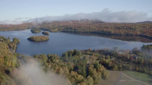 Drone footage of a tranquil lake surrounded by vibrant autumn forests, featuring small scenic island