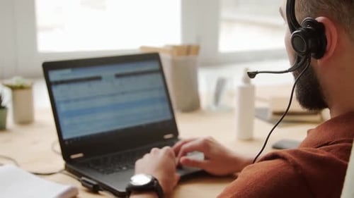 Man Types on Laptop with Headset
