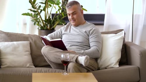 Man Relaxing on Sofa Reading Book with Wine