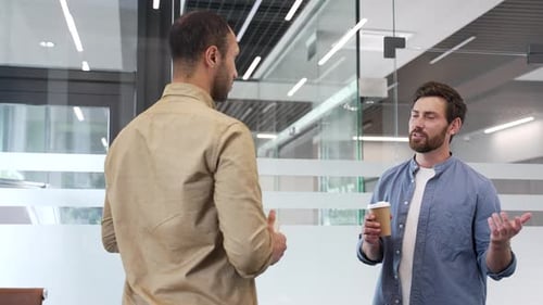 Two co-workers engaging in casual discussion while standing in modern office. Colleagues have friend