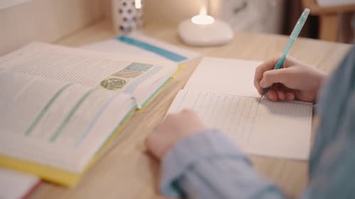 Student Writes in Notebook at Desk Indoors