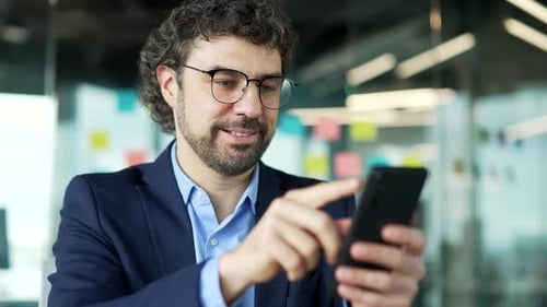 Confident businessman is using phone at workplace in business office. Man worker works on mobile