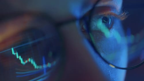 Trader Wearing Glasses is Working on Laptop Computer Screen with Stock Market Charts and Bitcoin BTC