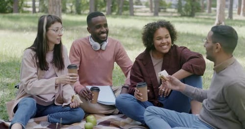 Happy Young People Friends Enjoying Picnic in Park Eating Sandwiches and Drinking Coffee Clinking