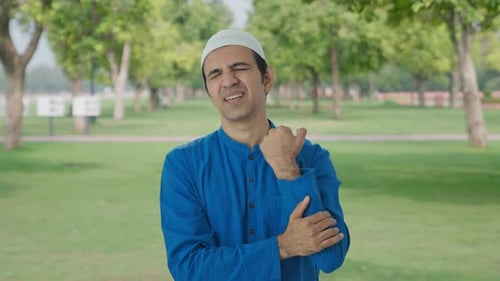 Sick Muslim man suffering from hand pain in park
