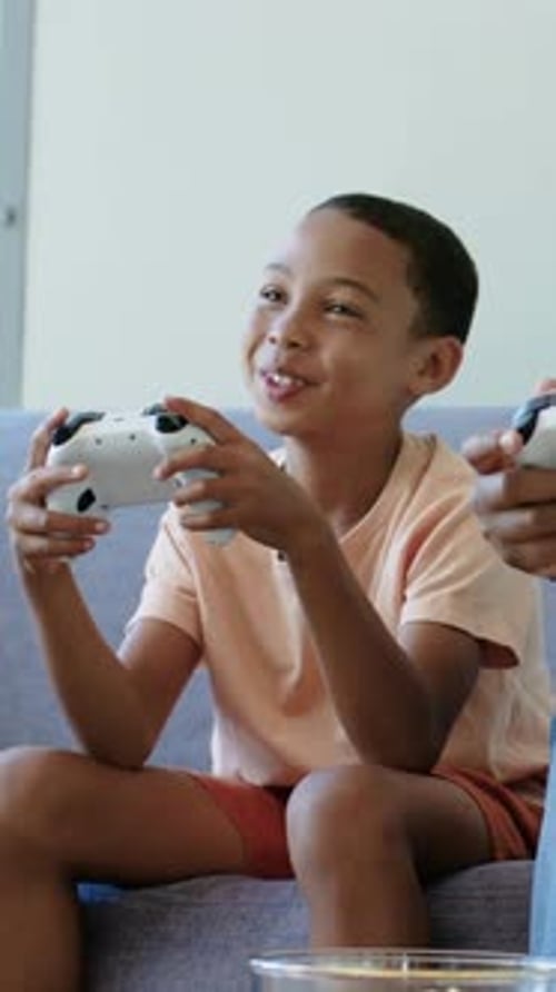Vertikales Video: Als Reaktion auf den Spielstart lehnt sich der Junge und lenkt das weiße Pad auf dem Sofa in pfirsichfarbenem T-Shirt