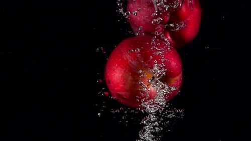 Roter Apfel in Zeitlupe, der unter Wasser fällt, auf schwarzem Hintergrund