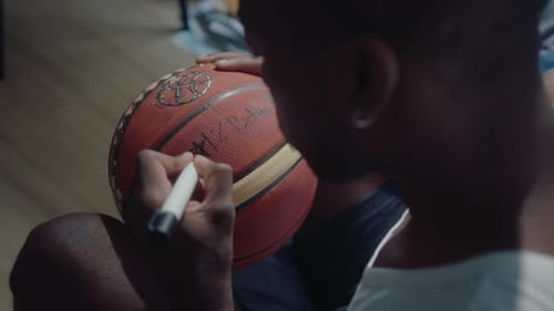 African American Basketball Player Writing a Sign on Ball