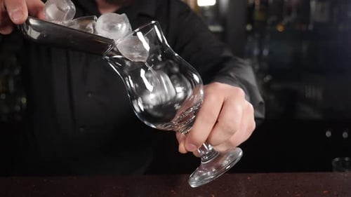 Bartender Putting Ice Cubes Into Transparent Glass Making Craft Cocktail on Bar Counter Making Fresh