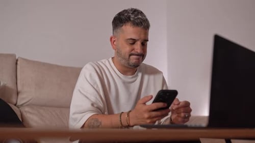 Man texting on smartphone in front of laptop