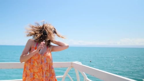 Sexy female in an airy dress seductive dances on wooden pier with sea horizon on vacation in summer
