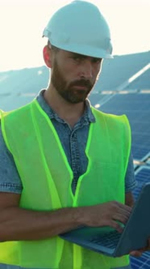 A Construction Worker Uses a Laptop Onsite Where Solar Panels Promote Energy Efficiency