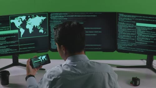 Homme asiatique travaillant avec un téléphone portable tout en écrivant du code avec plusieurs écrans d'ordinateur en écran vert