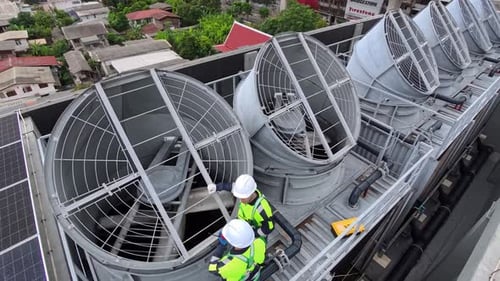 Workers inspect rooftop cooling system at commercial building site in midmorning