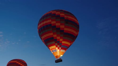 Multicolored hot air balloons with people inside them in the air, still dark, slowly ascending