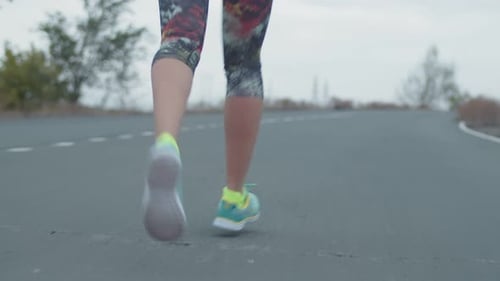 Closeup of Women's Legs in Sneakers Running on Asphalt Outdoors Back View