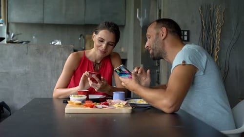 Couple at Table Looking at Phones and Eating