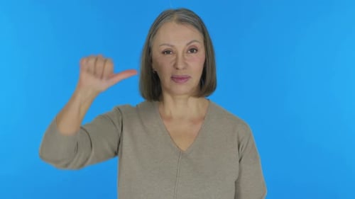 Vieille femme avec les pouces vers le bas sur fond bleu, portrait